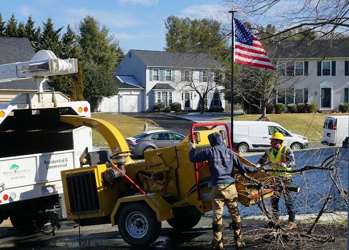 Two men are working on a tree chipper in front of a house
