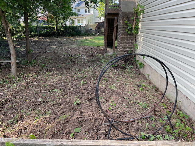 A hose is sitting in the dirt in front of a house.