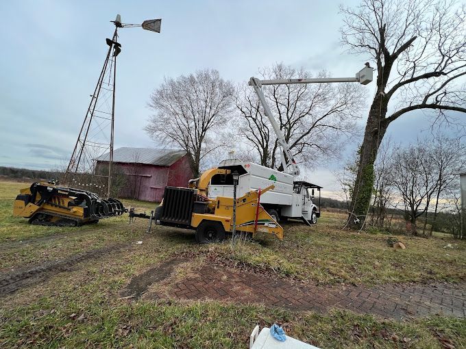A tree chipper is parked in a field next to a windmill.