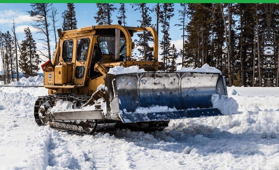 A bulldozer is clearing snow from a road in the woods.