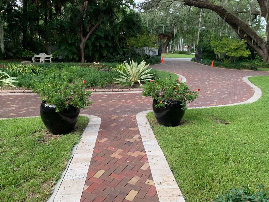 Brick pathway leading to a green lawn with trees and a white building in the background. Sunny day.