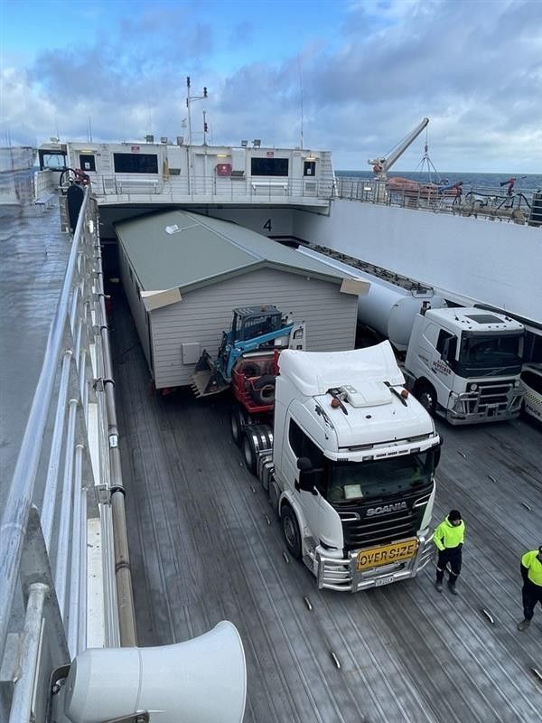 Trucks on a ferry’s car deck with a partially collapsed trailer roof and workers nearby Trucks on a ferry’s car deck with a partially collapsed trailer roof and workers nearby