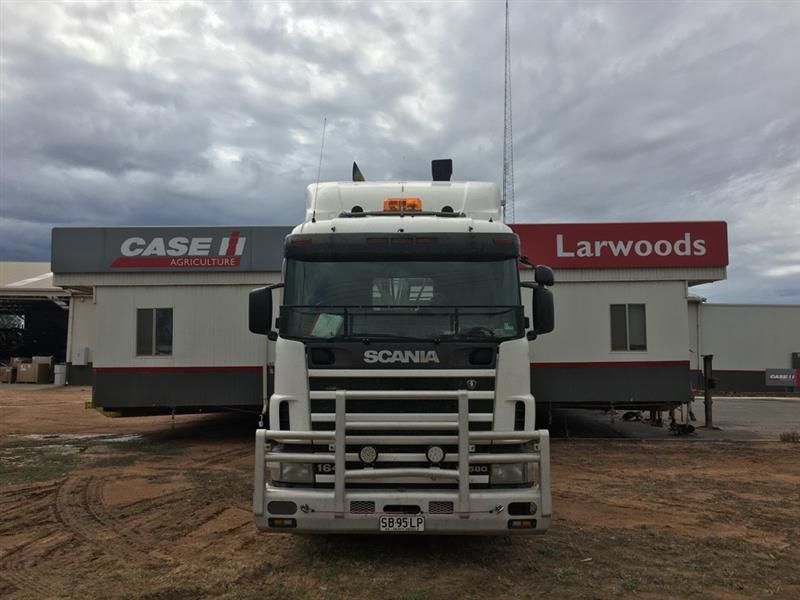 White Scania truck parked in front of Larwoods and Case IH buildings under a cloudy sky