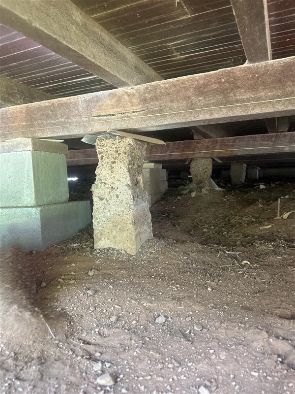 Crawl space under a wooden house with dirt floor, low beams, and stacked cinder blocks supporting a column. Crawl space under a wooden house with dirt floor, low beams, and stacked cinder blocks supporting a column.