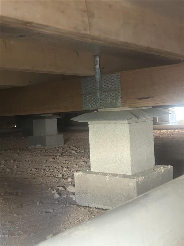 Underfloor concrete supports and a metal bracket beneath a wooden structure