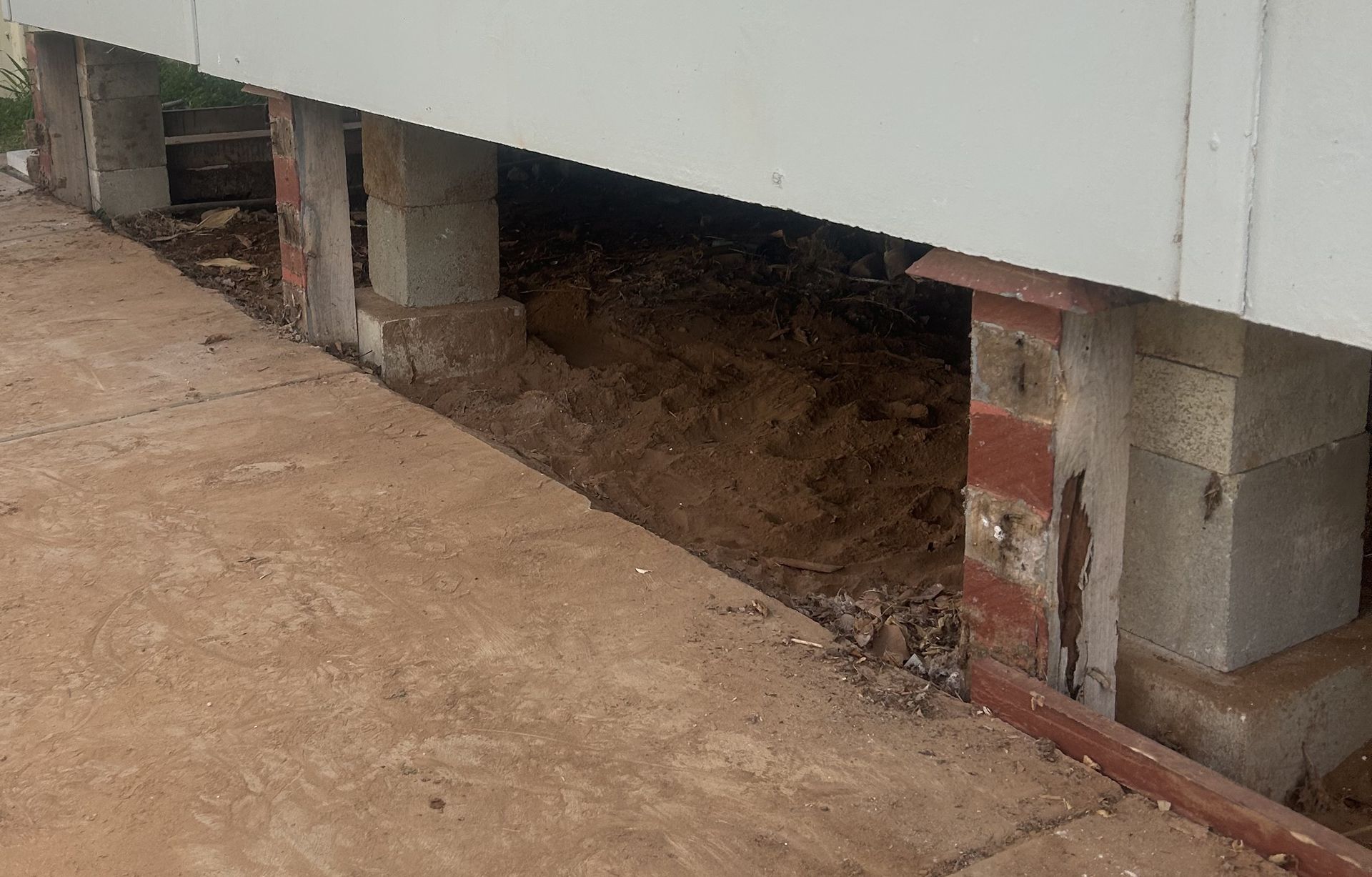 Crawlspace under a house with exposed brick supports and dirt ground beside a concrete walkway Crawlspace under a house with exposed brick supports and dirt ground beside a concrete walkway