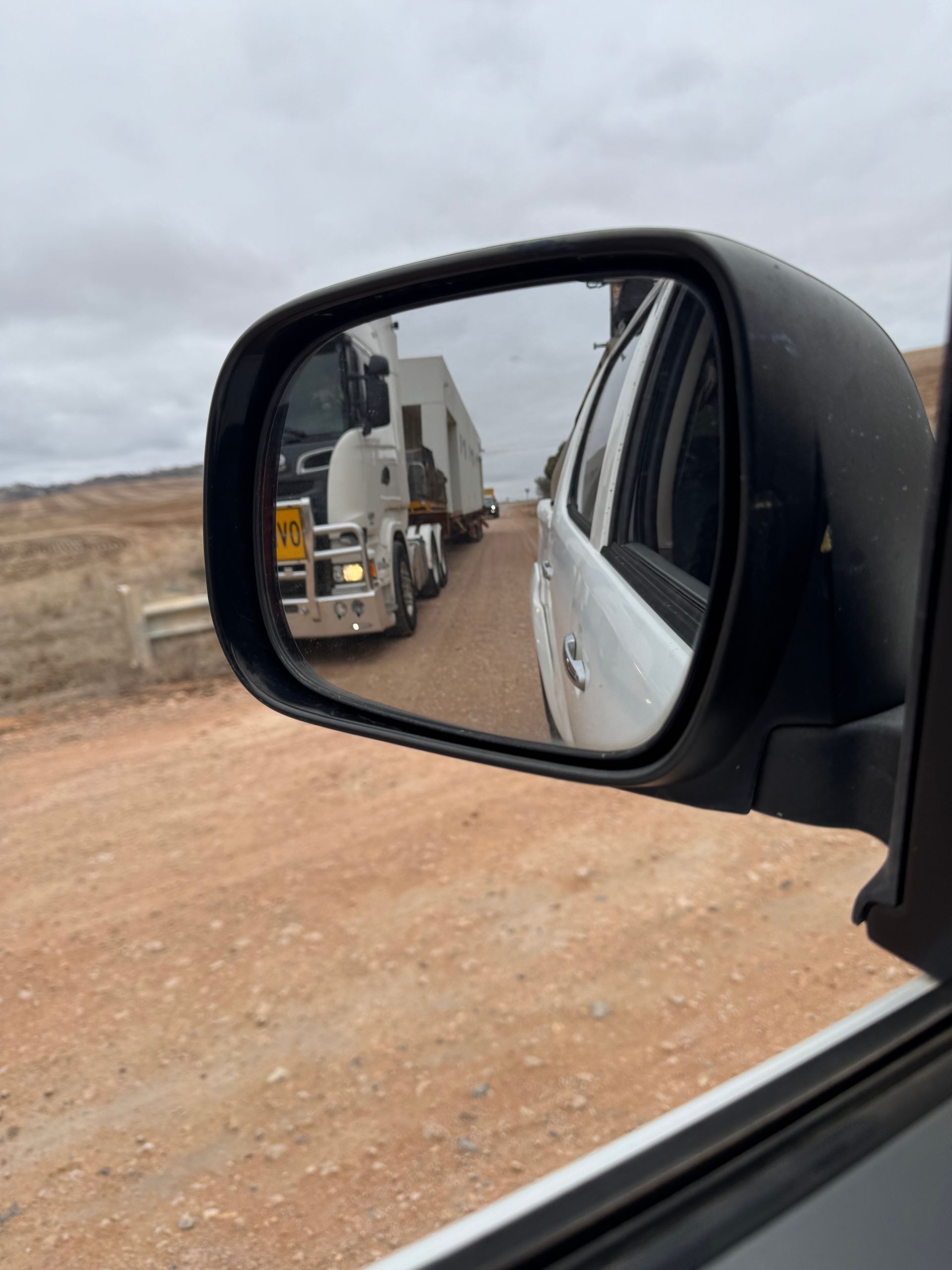 Truck reflected in car side mirror on a dusty road beside a cloudy landscape Truck reflected in car side mirror on a dusty road beside a cloudy landscape