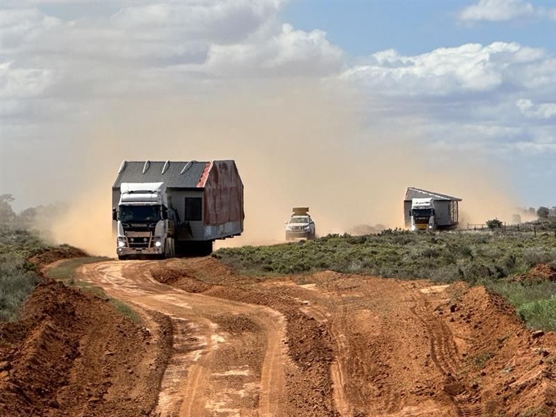 Two dump trucks driving on a dusty dirt road through a rural landscape under a cloudy sky Two dump trucks driving on a dusty dirt road through a rural landscape under a cloudy sky
