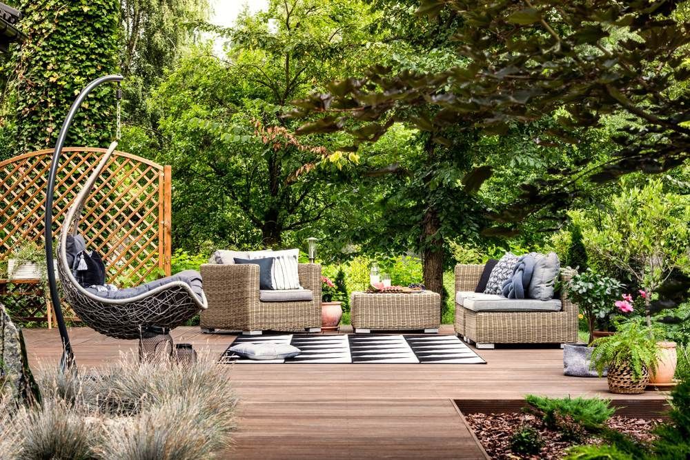 Hanging chair and geometric carpet on wooden patio with rattan garden furniture