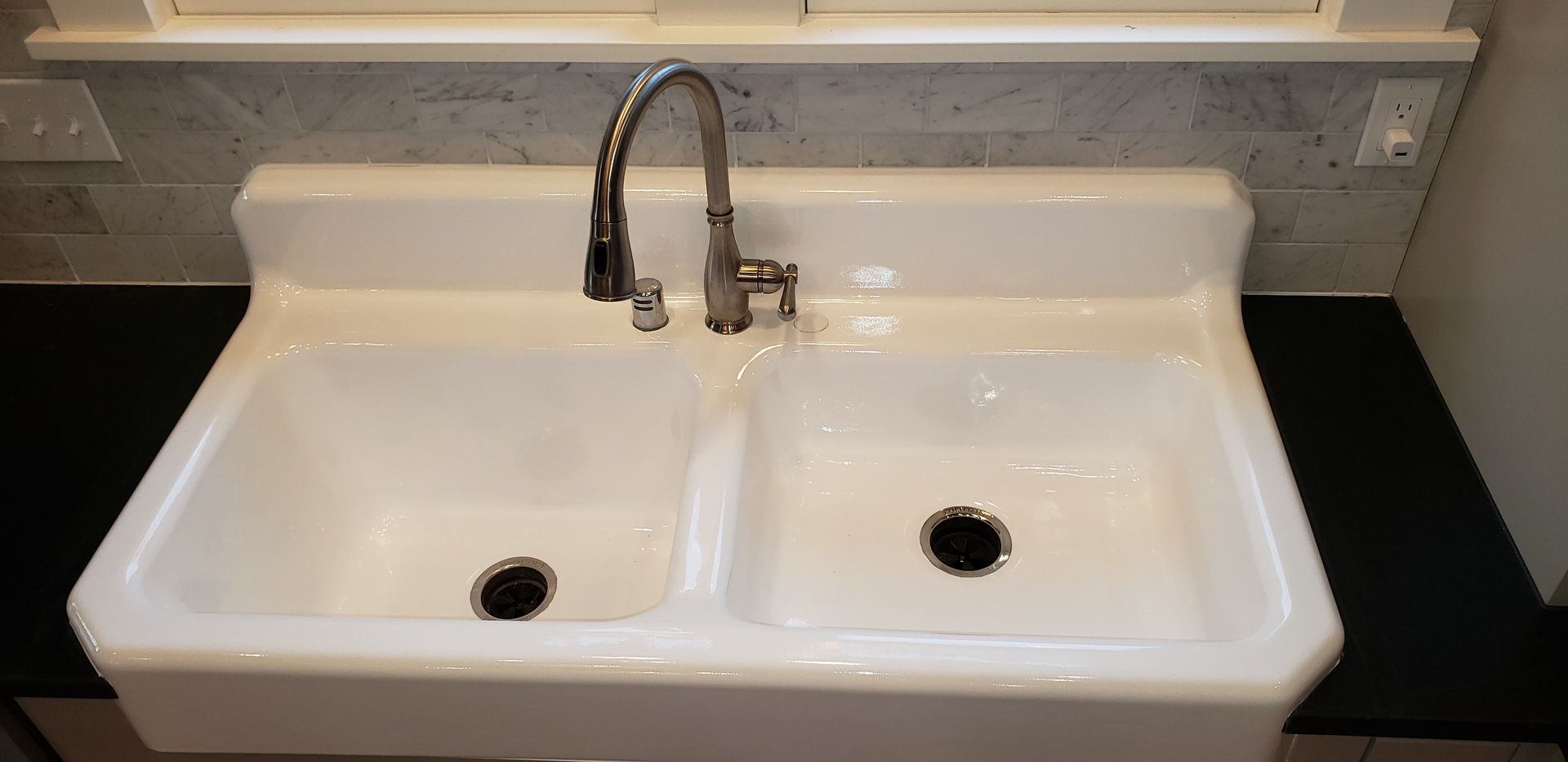 A white double sink with a chrome faucet against a gray tiled backsplash.