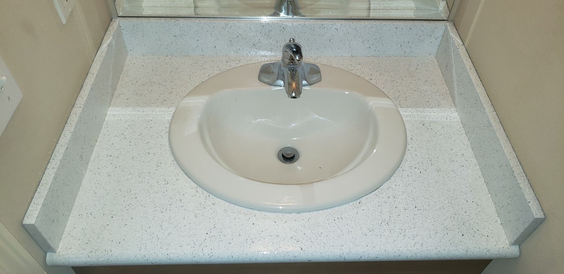 A bathroom sink with a white speckled countertop and a silver faucet.