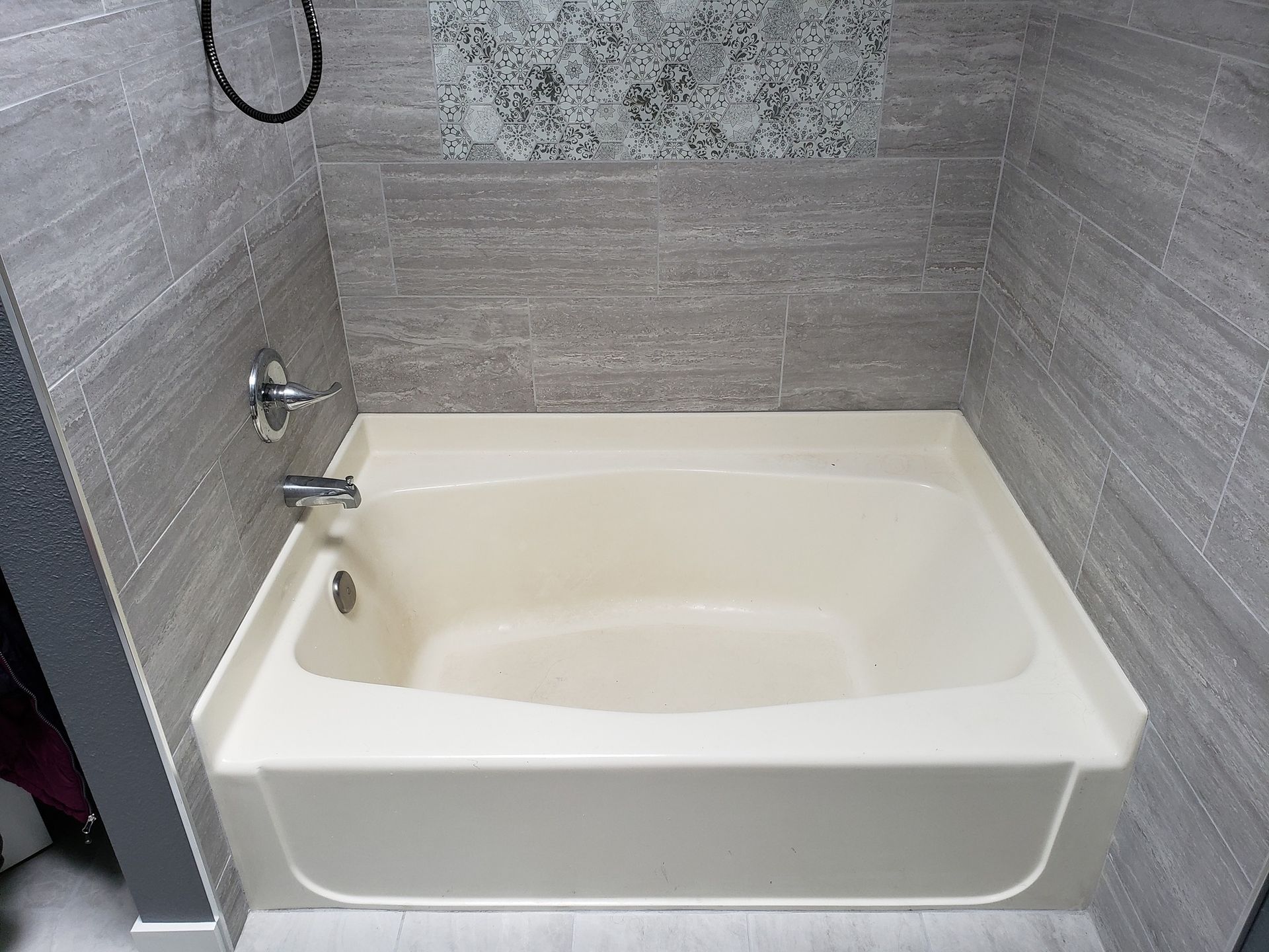 Bathtub in a bathroom with gray tiled walls, a silver faucet, and a decorative glass tile accent.