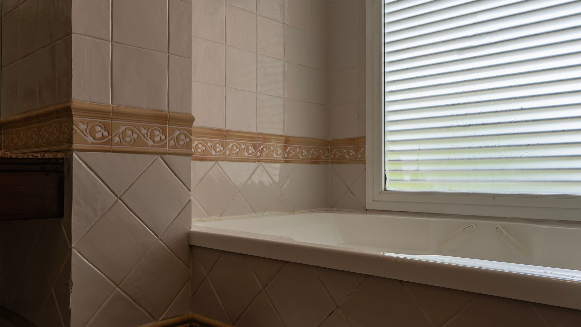 A white rectangular bathtub in the corner of a bathroom with beige tiled walls.