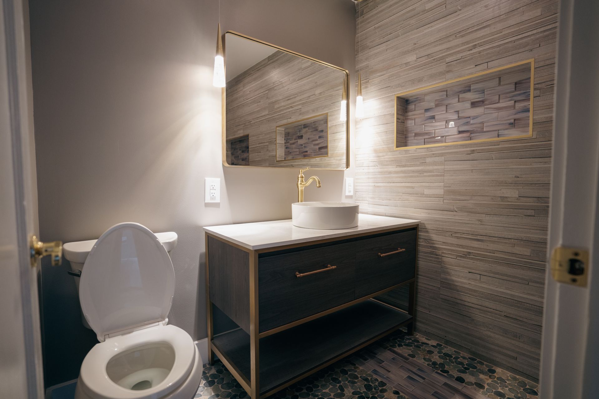 Modern powder room with gray vanity, gold accents, and textured stone tile walls.