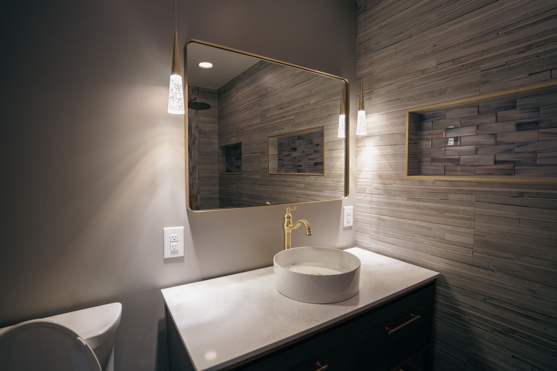 Modern bathroom with a gold-framed mirror, vessel sink, and decorative tile.
