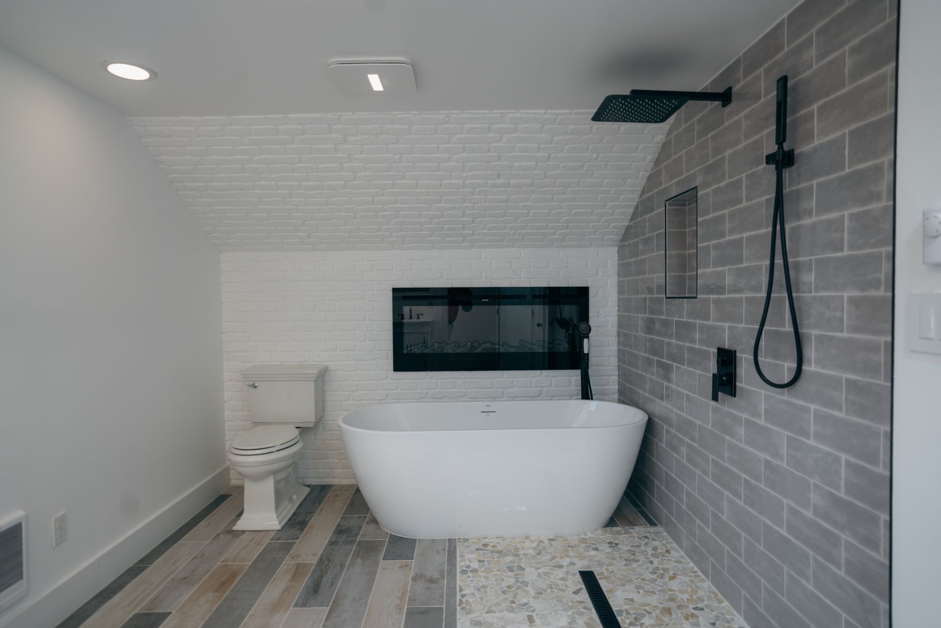 Modern bathroom with a white tub, grey brick wall, and a black showerhead.
