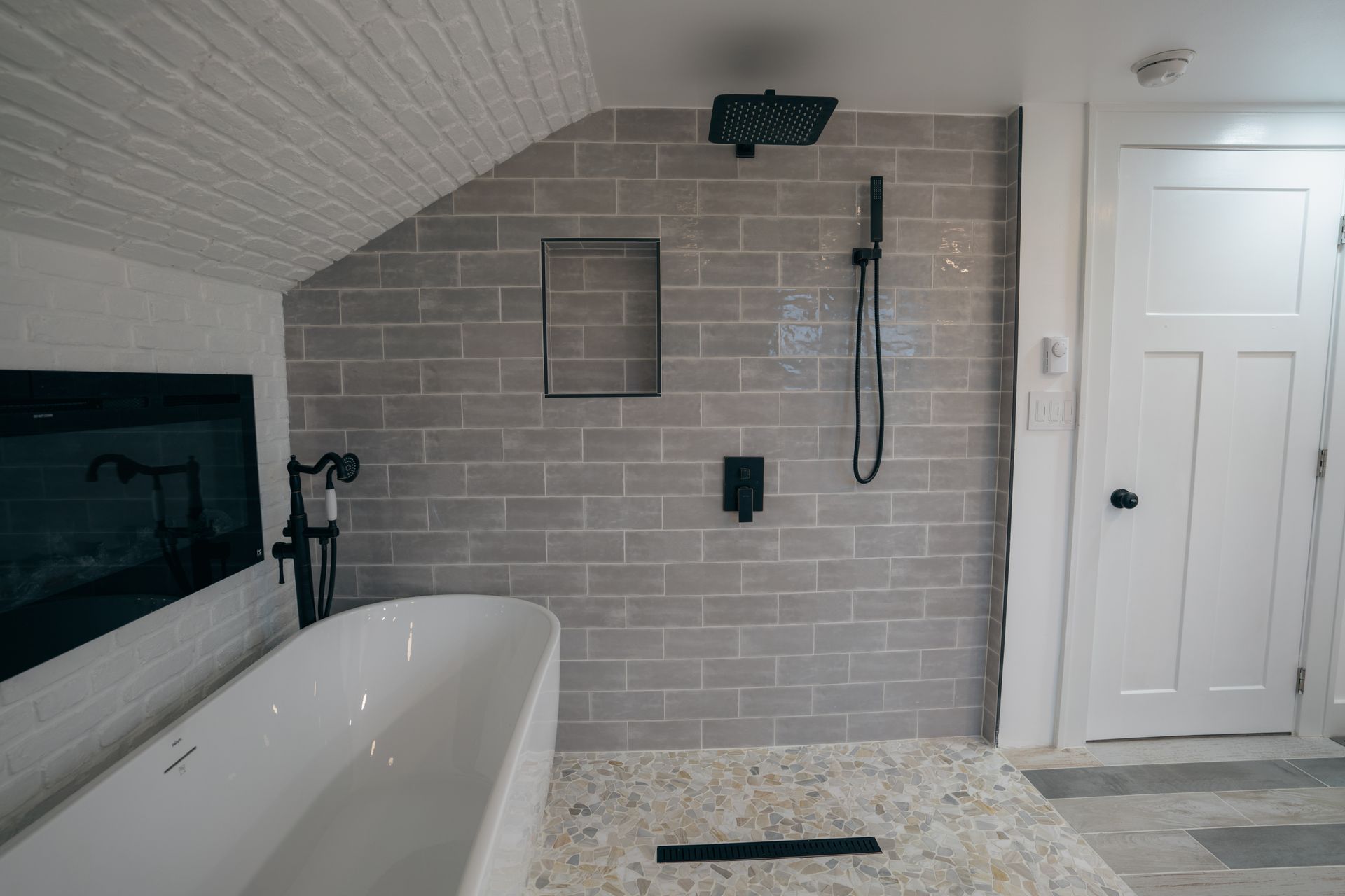 Bathroom with a white bathtub, gray tiled shower, and a white door.