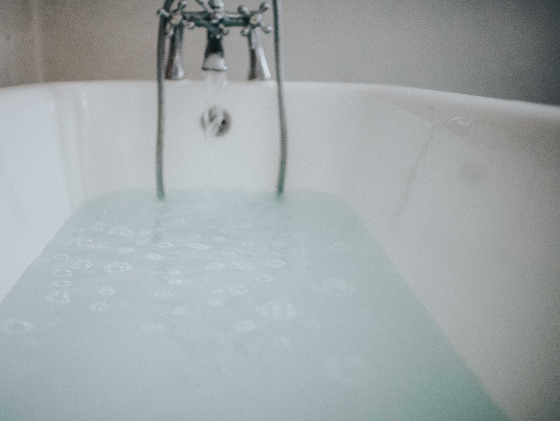 Bathtub filled with water, faucet and handles visible.