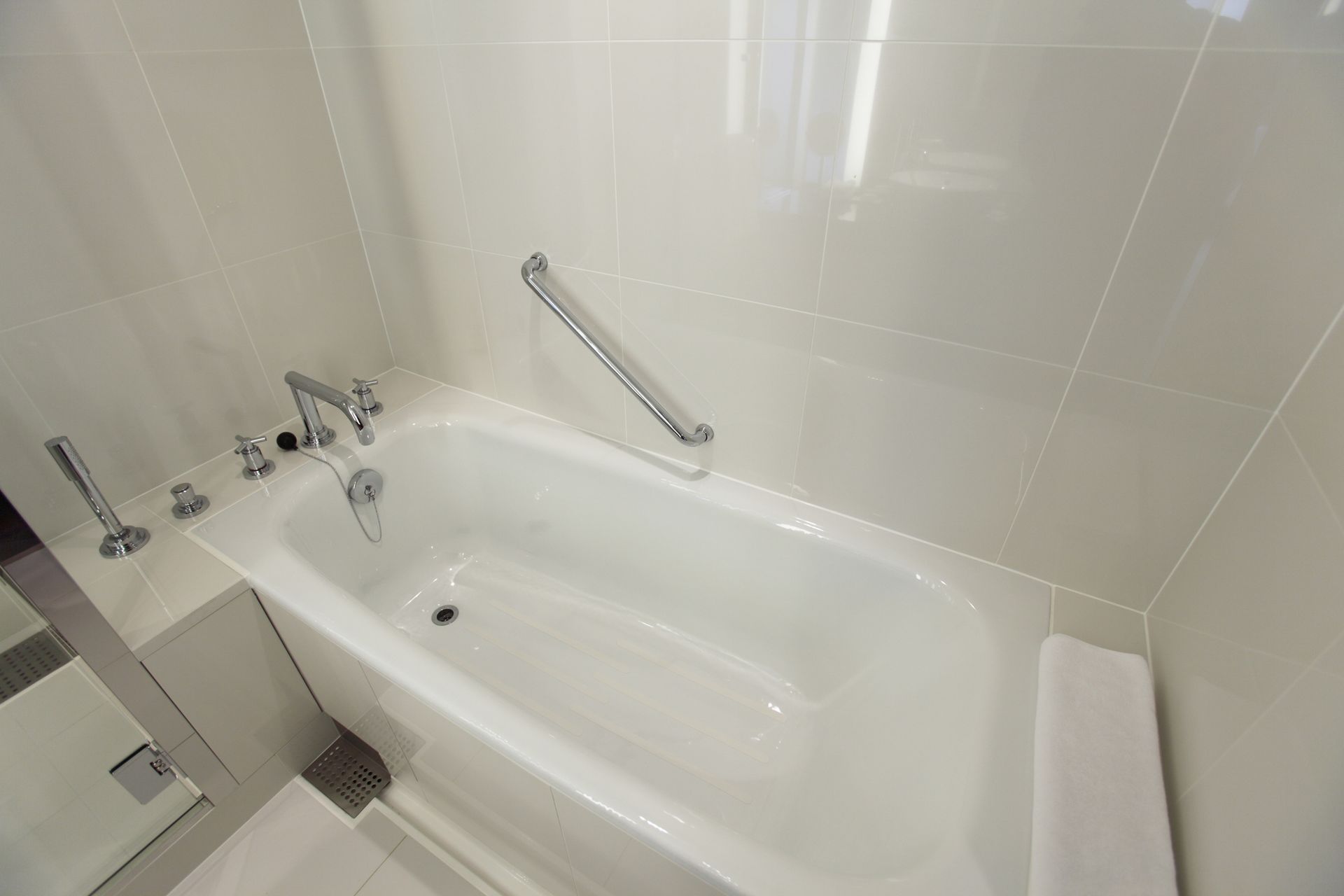 White bathtub with chrome fixtures and grab bar in a tiled bathroom.
