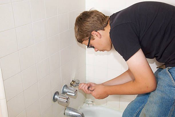 A plumber fixes a leaking bathtub fixture using a wrench.