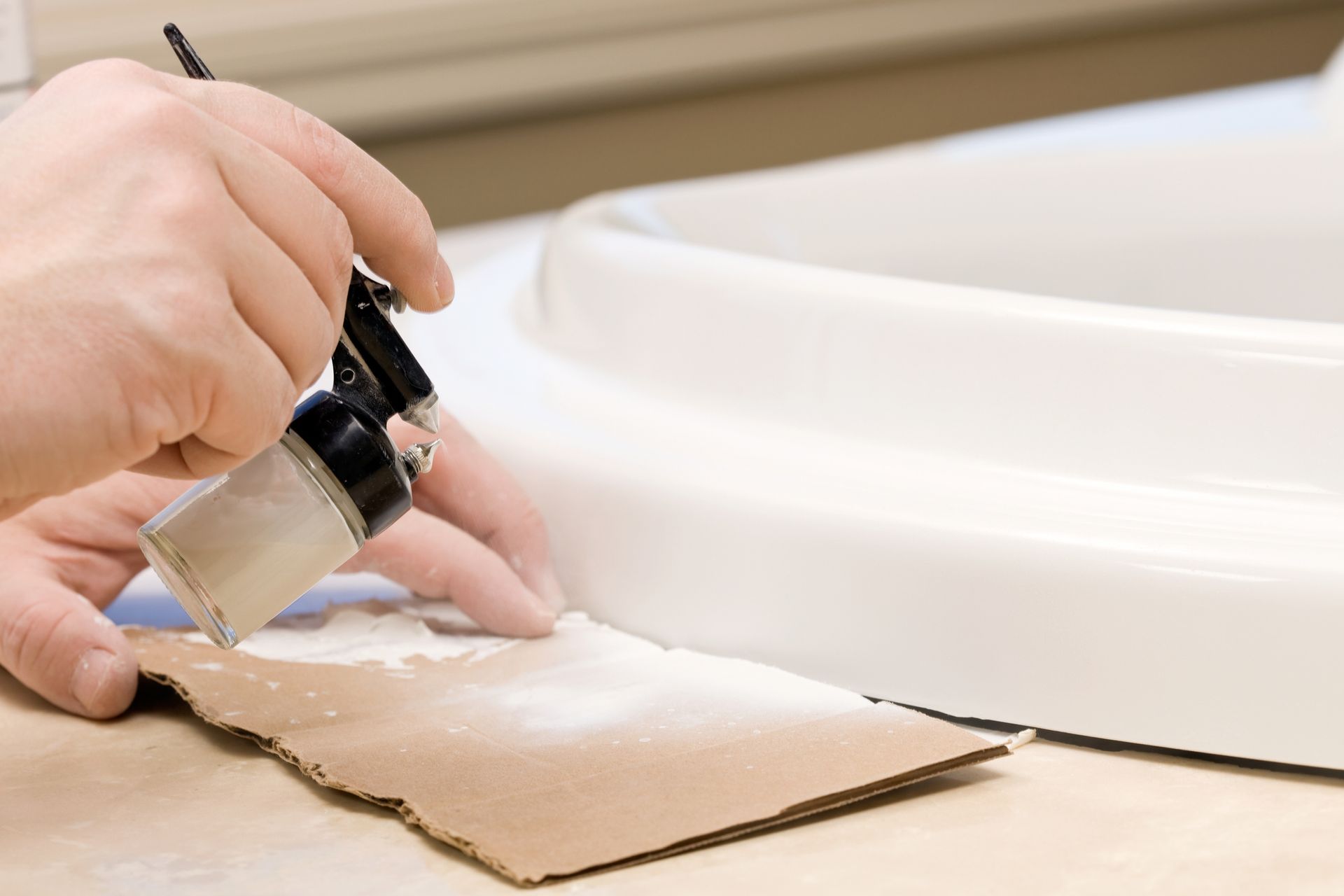 Worker painting with an airbrush to color match the repair of a fiberglass bathtub.