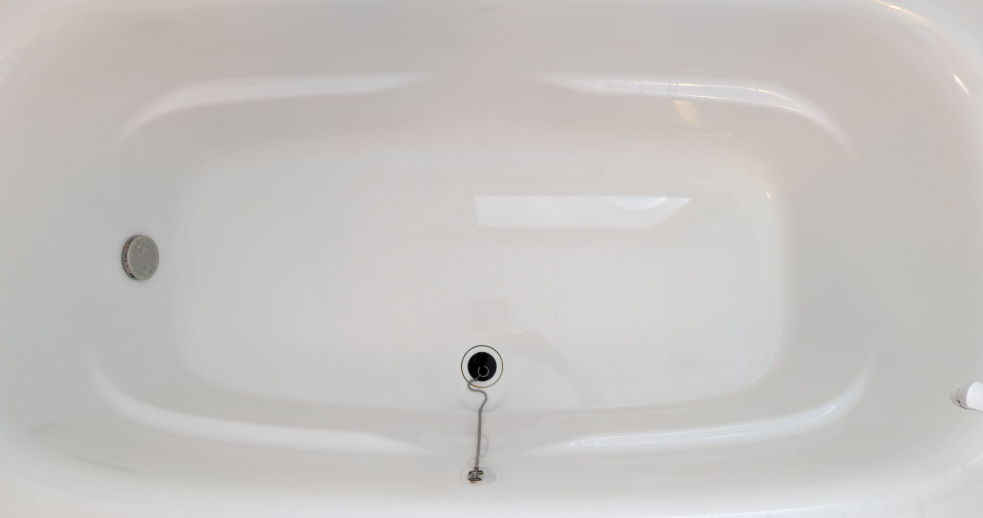 Empty white bathtub with a drain and chain plug.
