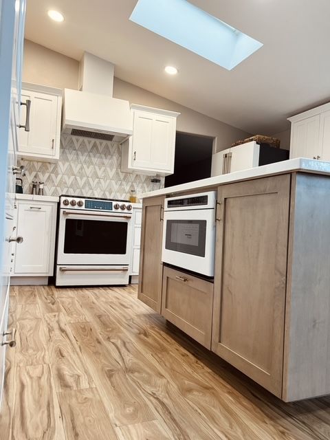 Kitchen with wood floors, white and gray cabinets, stove, microwave, and skylight.