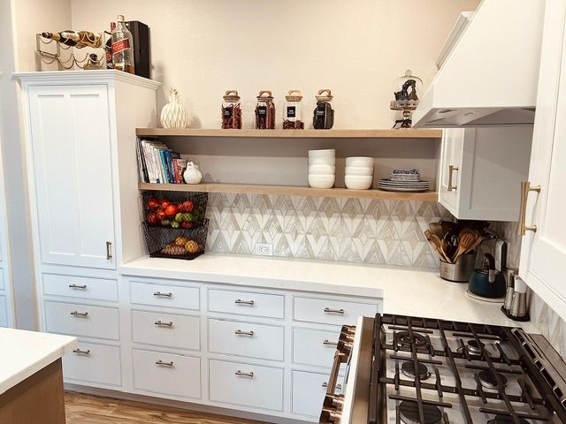 White kitchen with built-in drawers, shelves, and cabinets. A gas range and decorative items are present.