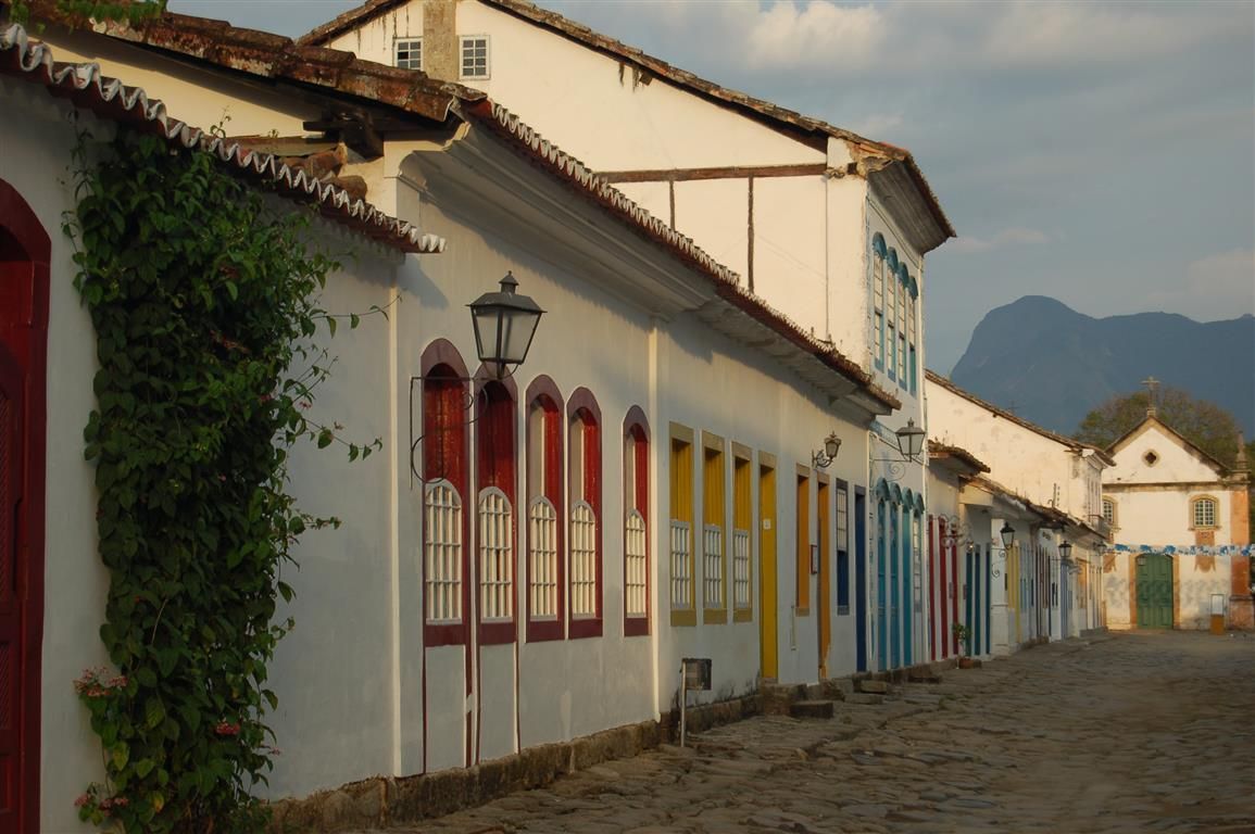 Fileira de edifícios coloniais coloridos com molduras de janelas vibrantes ao longo de uma rua de paralelepípedos em Paraty, Brasil.