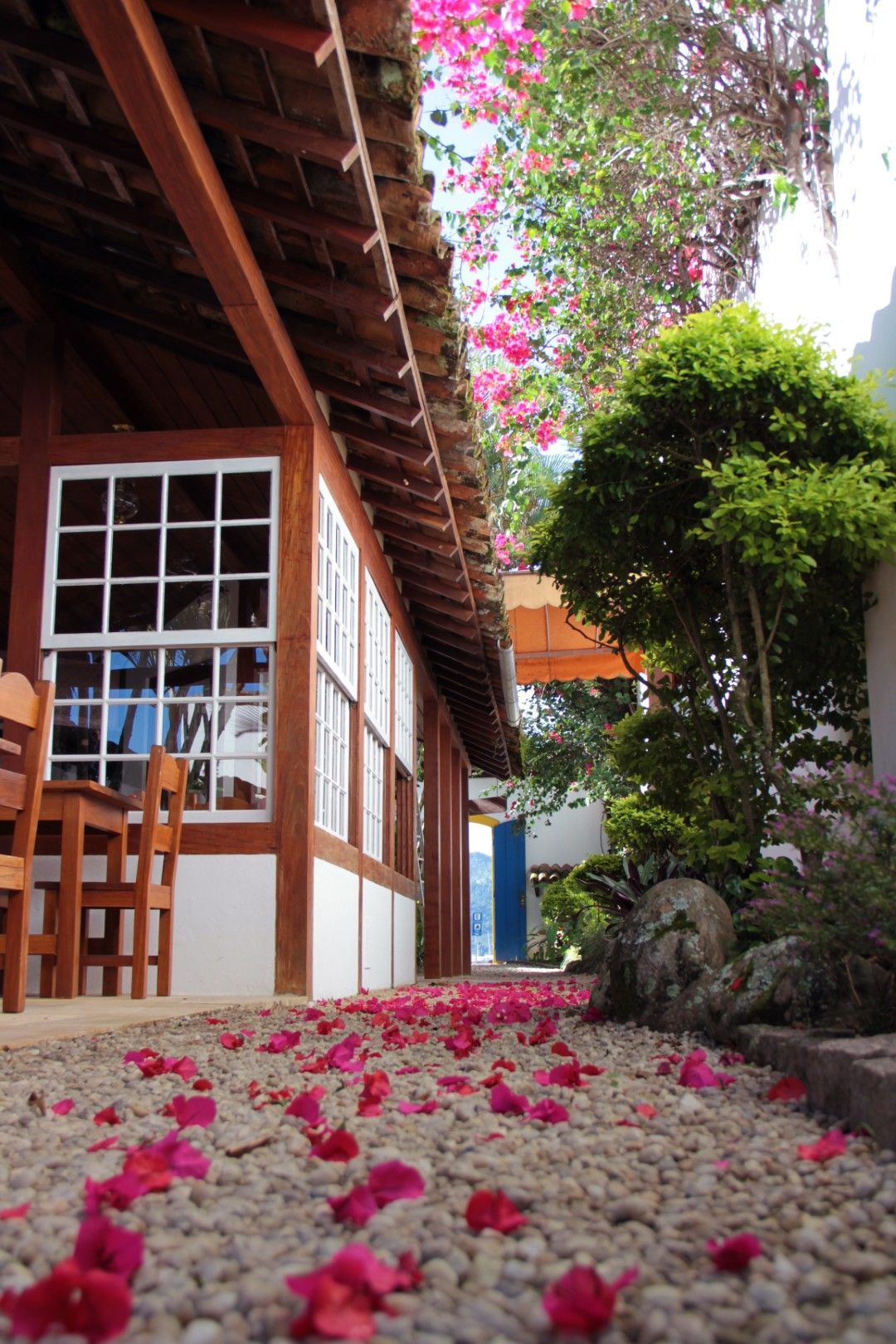 Um prédio com telhado de madeira e janelas com molduras brancas. Pétalas de flores cor-de-rosa cobrem o caminho de seixos.