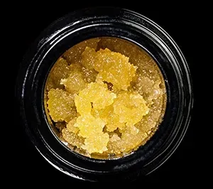 Open black jar filled with golden, crystalline cannabis concentrate.