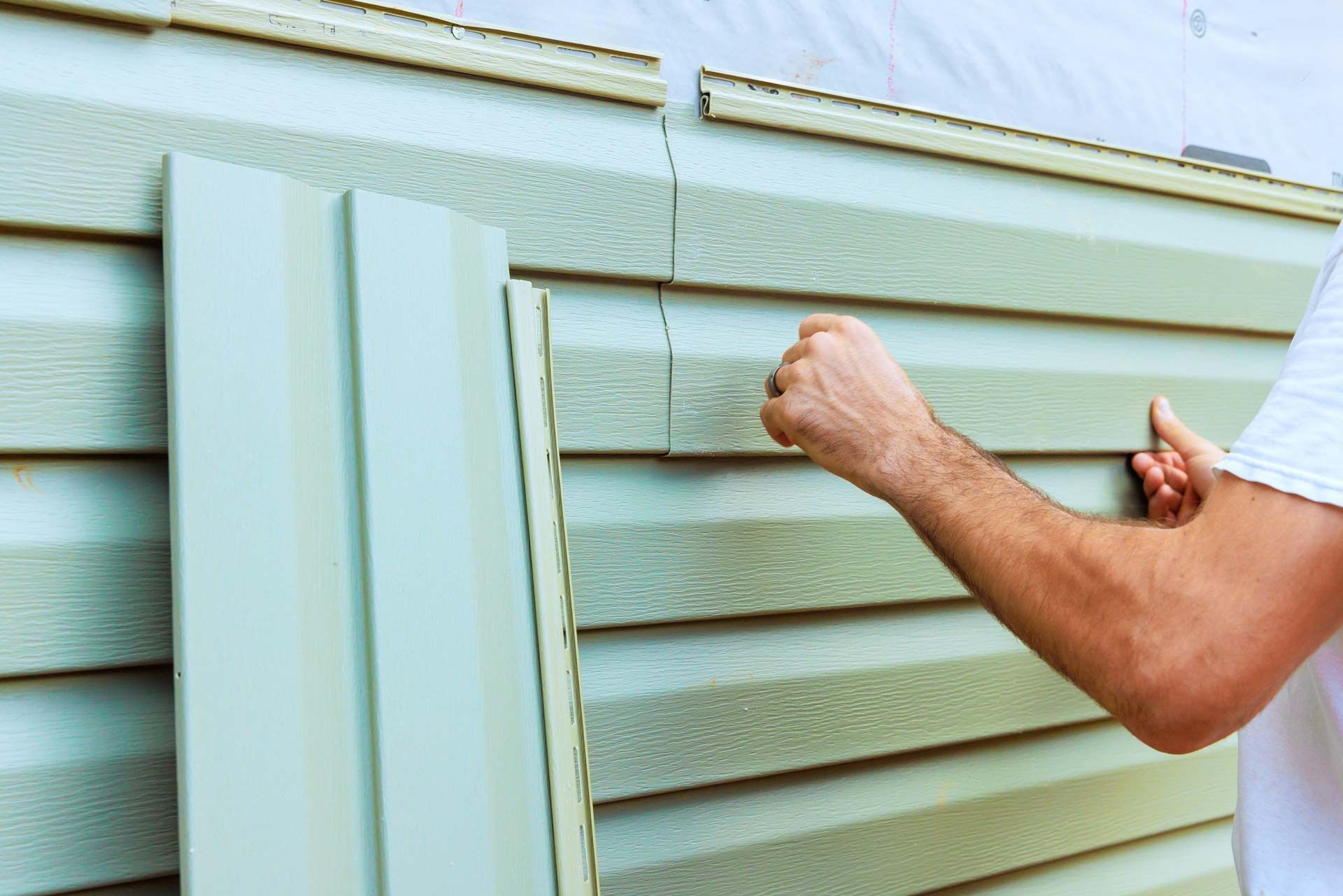 A person installing light green horizontal vinyl siding on an exterior wall.