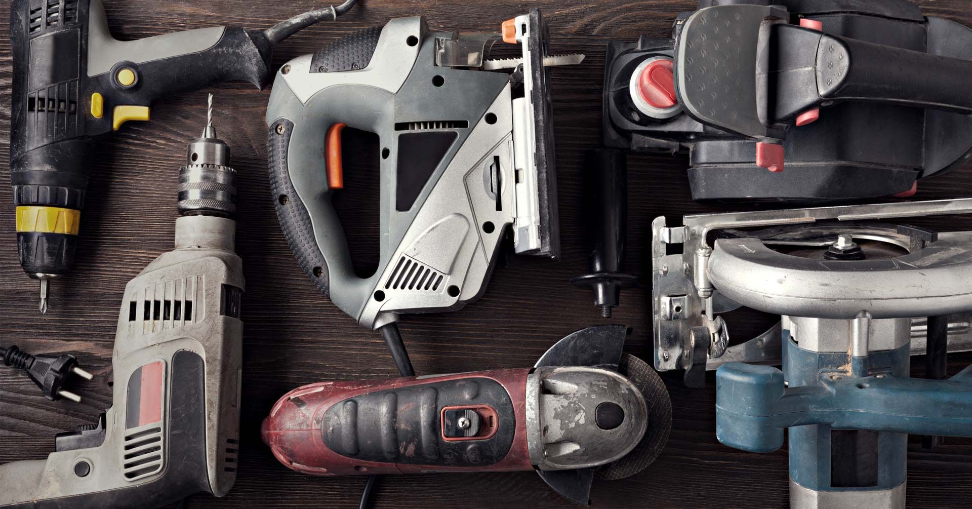 A top-down view of various corded power tools, including a drill, jigsaw, sander, angle grinder, and circular saw.