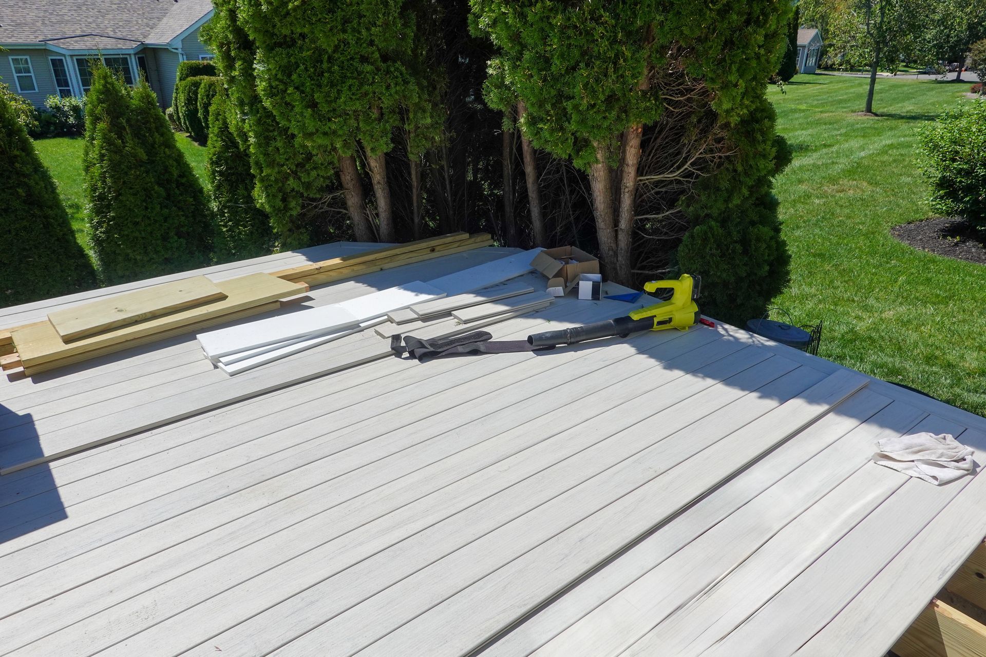 A light-colored wooden deck under construction, with a yellow power tool and building materials lying on the surface.