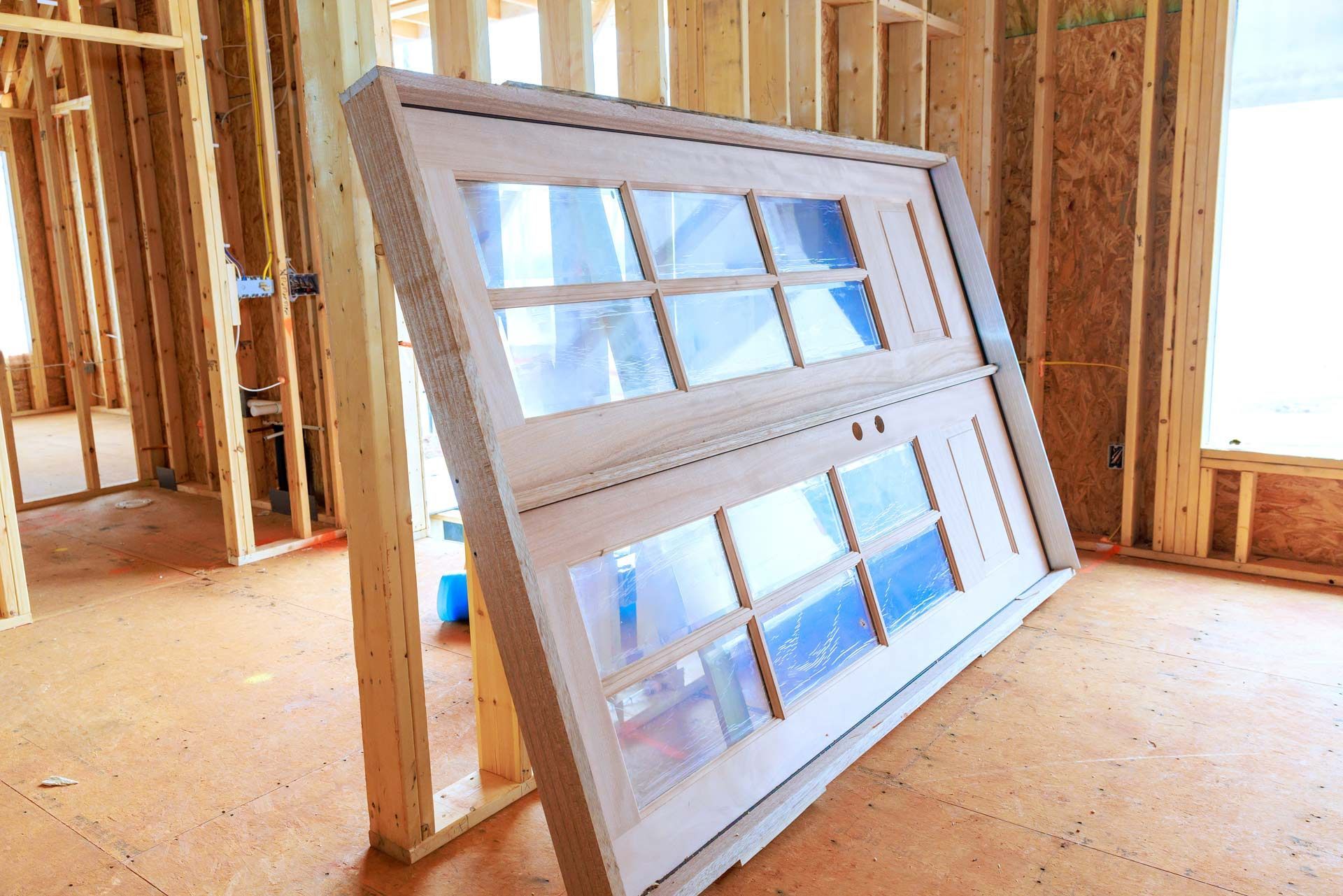 A white, multi-pane window unit leans against wooden wall studs in a room under construction.