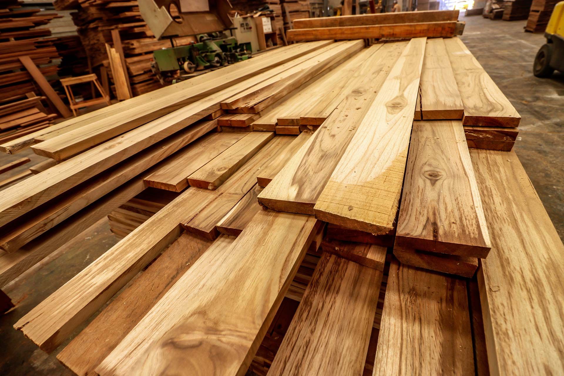 Stacks of light-brown wooden planks and timber boards arranged in a lumber yard or workshop.