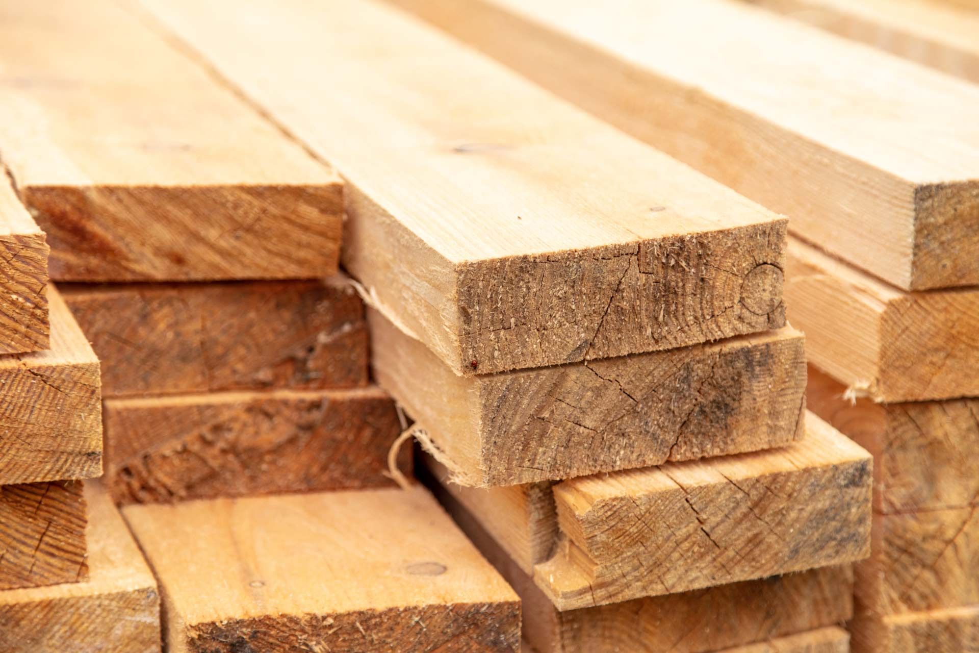 A stack of rough-cut, light-brown wooden boards piled in a lumber yard.