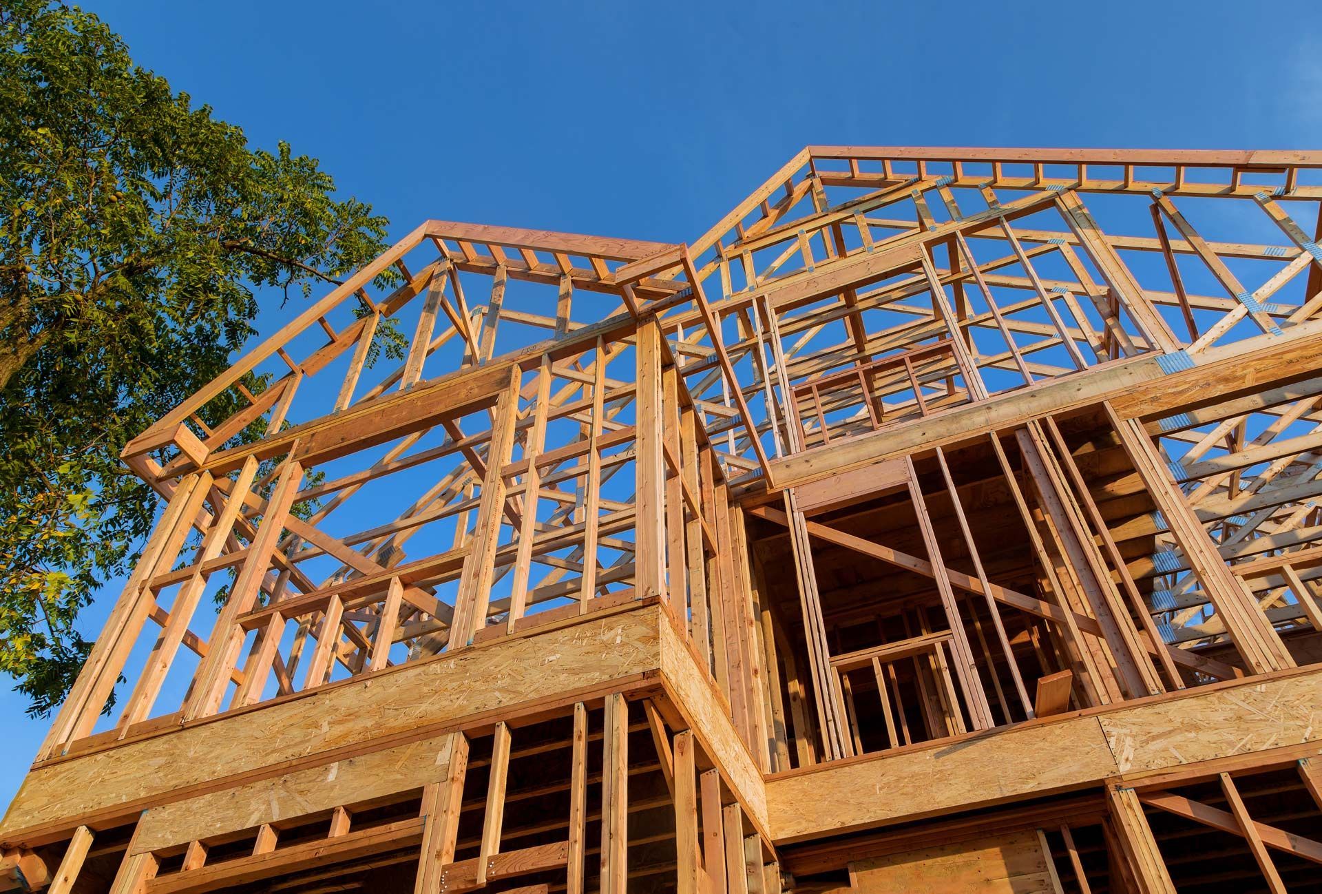 The wooden structural framing of a multi-story house under construction against a clear blue sky.