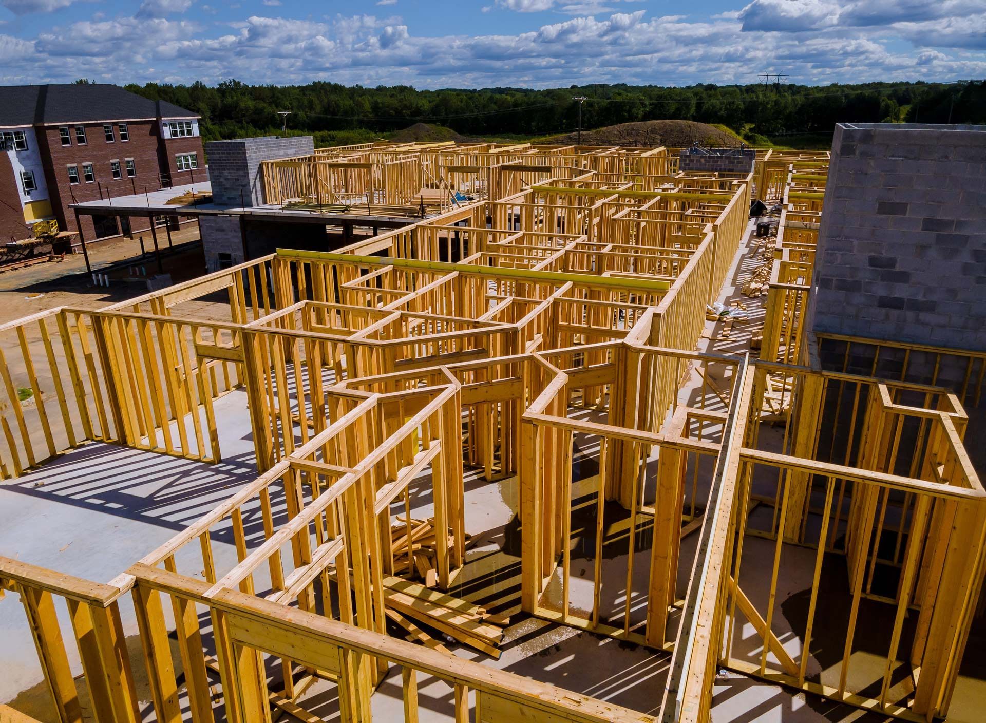 An aerial view of a building under construction, featuring wooden wall frames on a concrete slab against a blue sky.