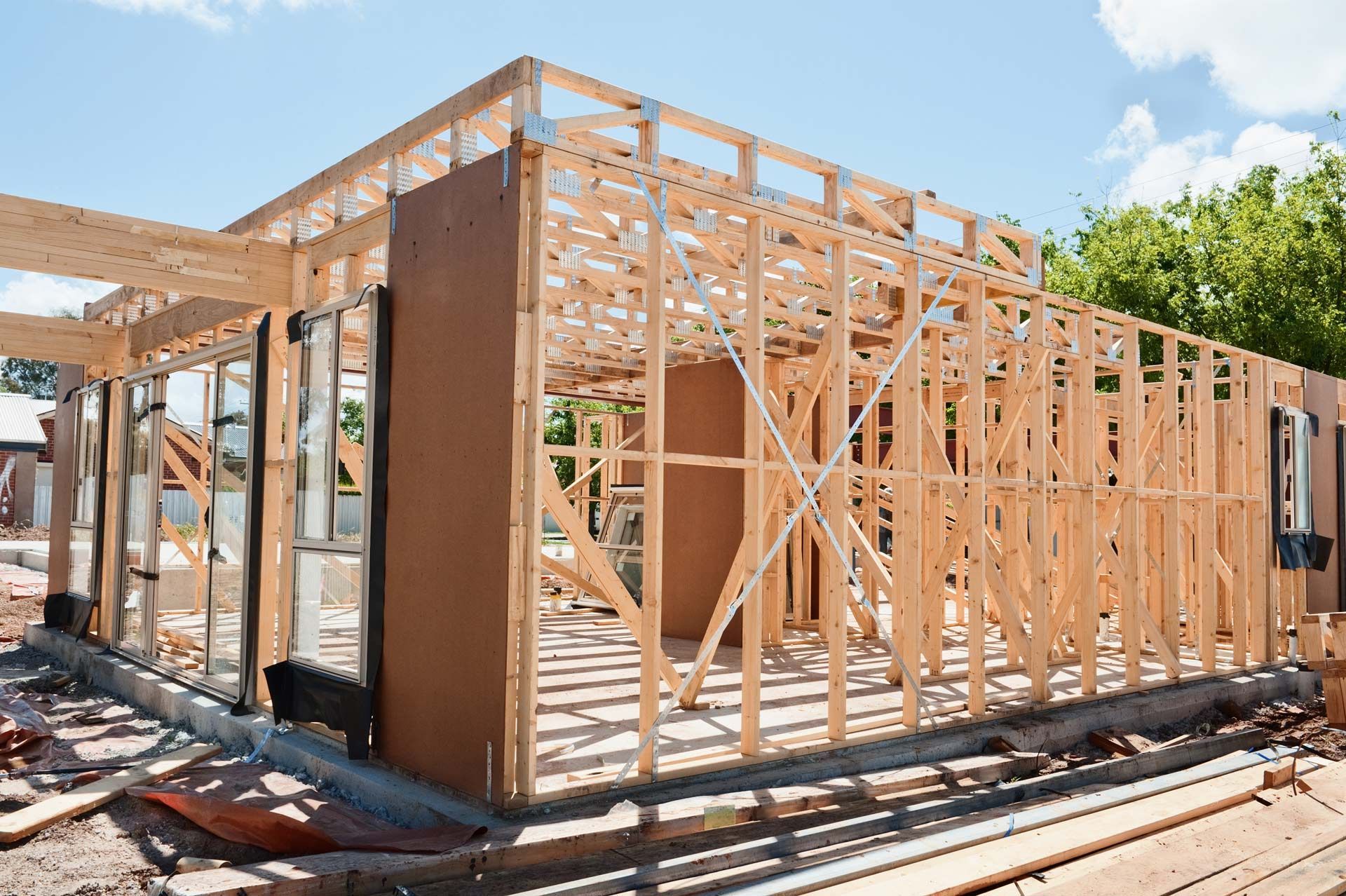 The wooden frame of a new house under construction on a concrete foundation under a sunny sky.