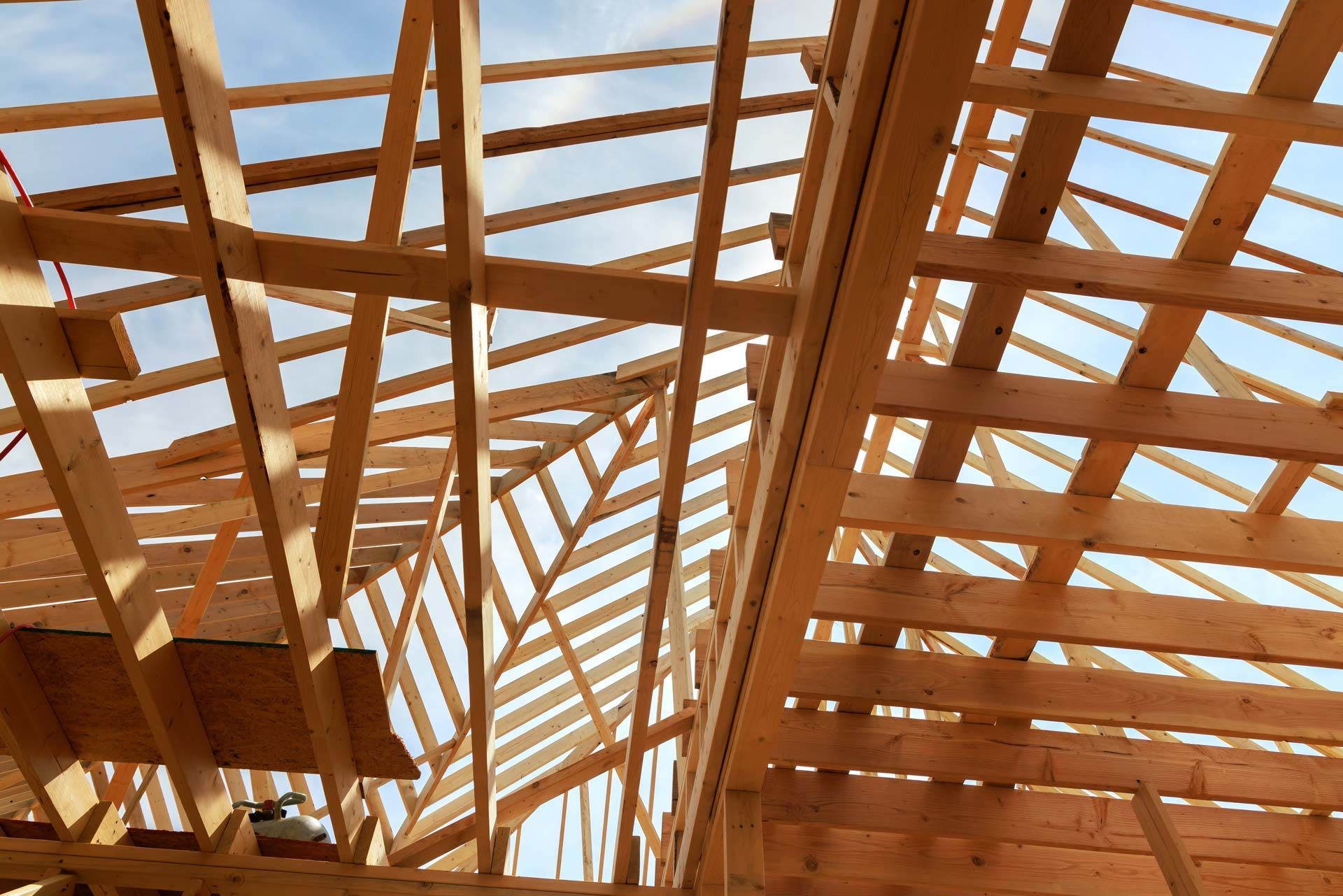 The wooden framing of a building's roof under construction against a clear blue sky.