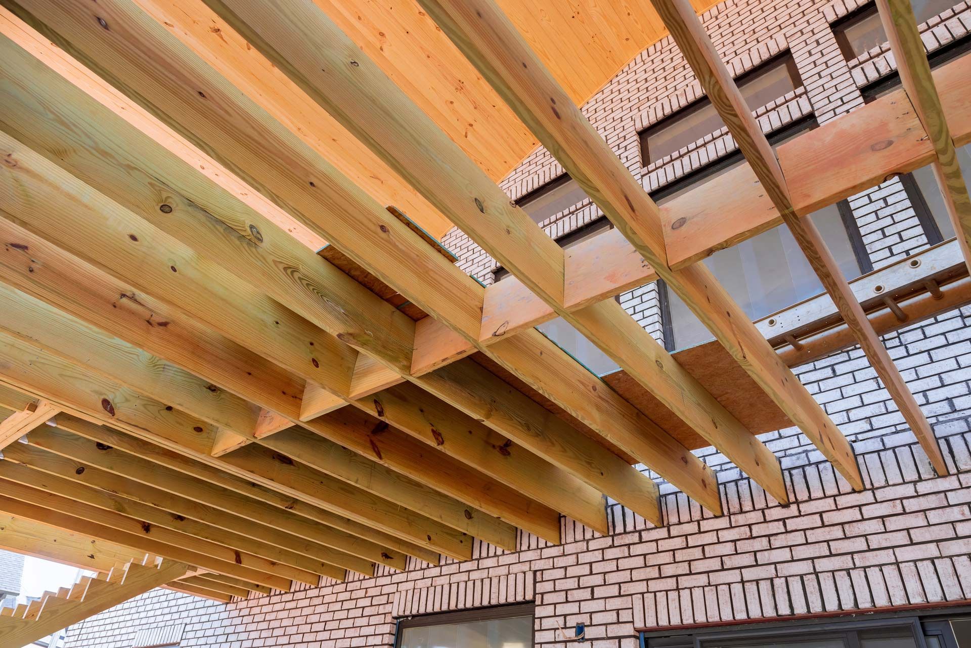 A low-angle view of unfinished wooden rafters and beams extending from the brick exterior wall of a residential building.