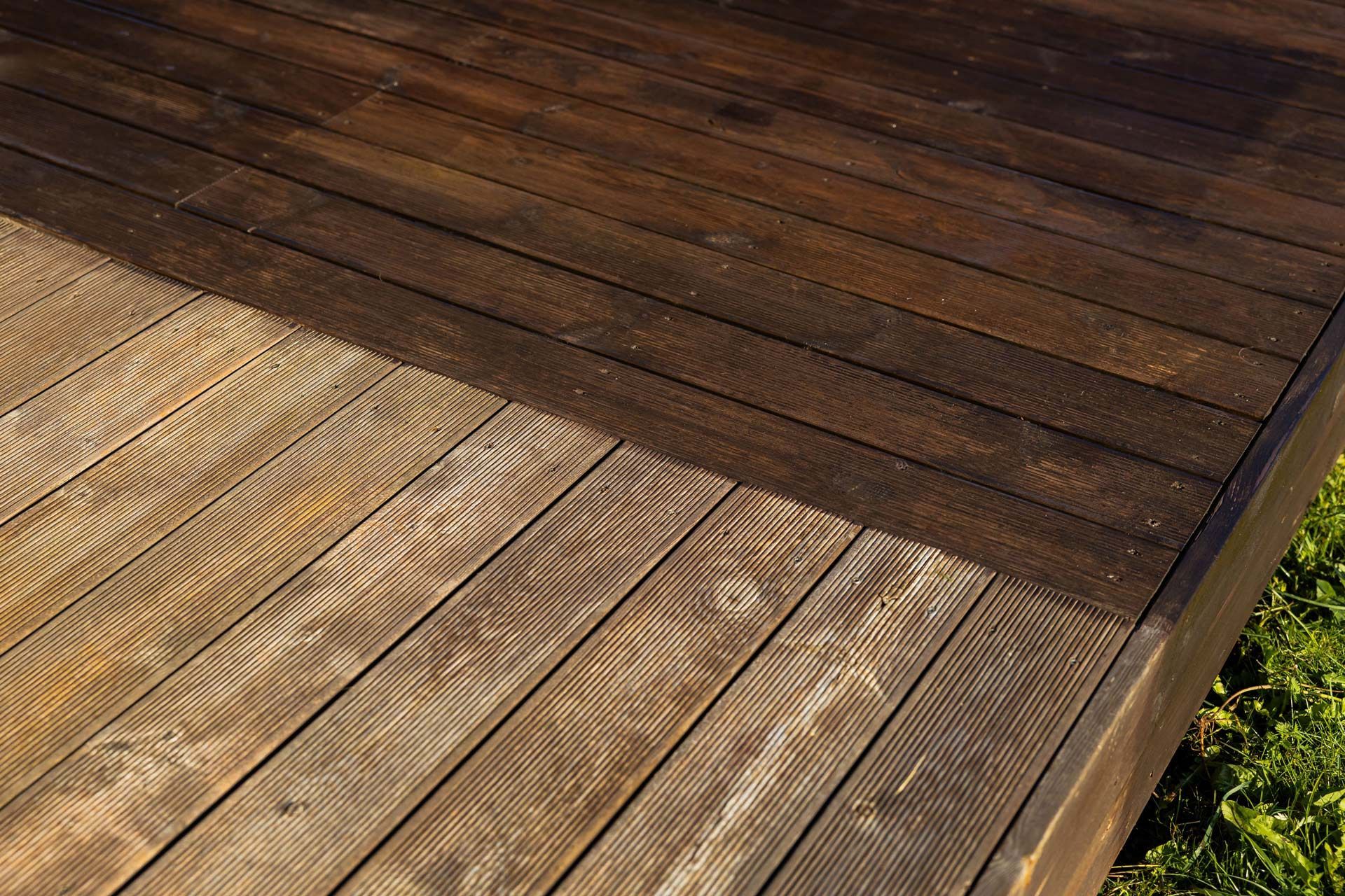 A wooden deck showing a sharp contrast between a weathered, light-colored side and a newly stained, dark-brown section.