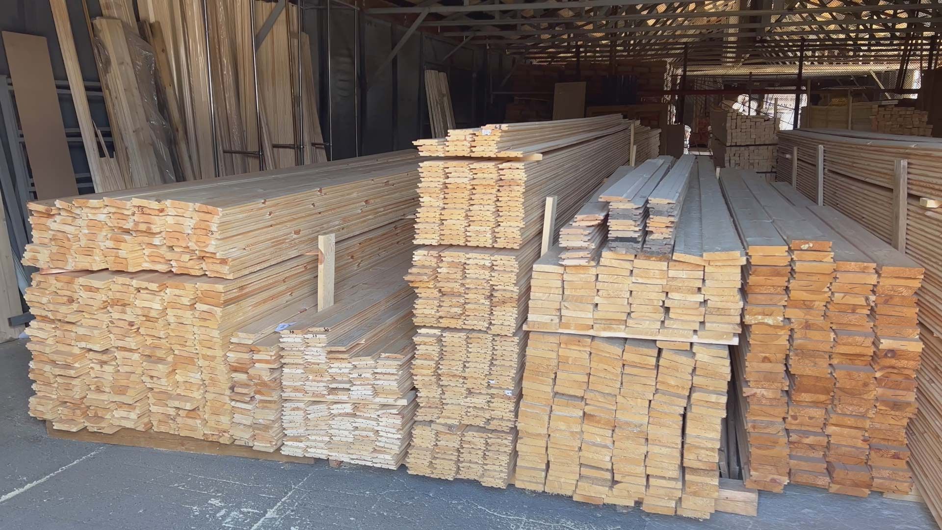 Several organized stacks of cut lumber arranged in rows within a large, covered warehouse or lumberyard.