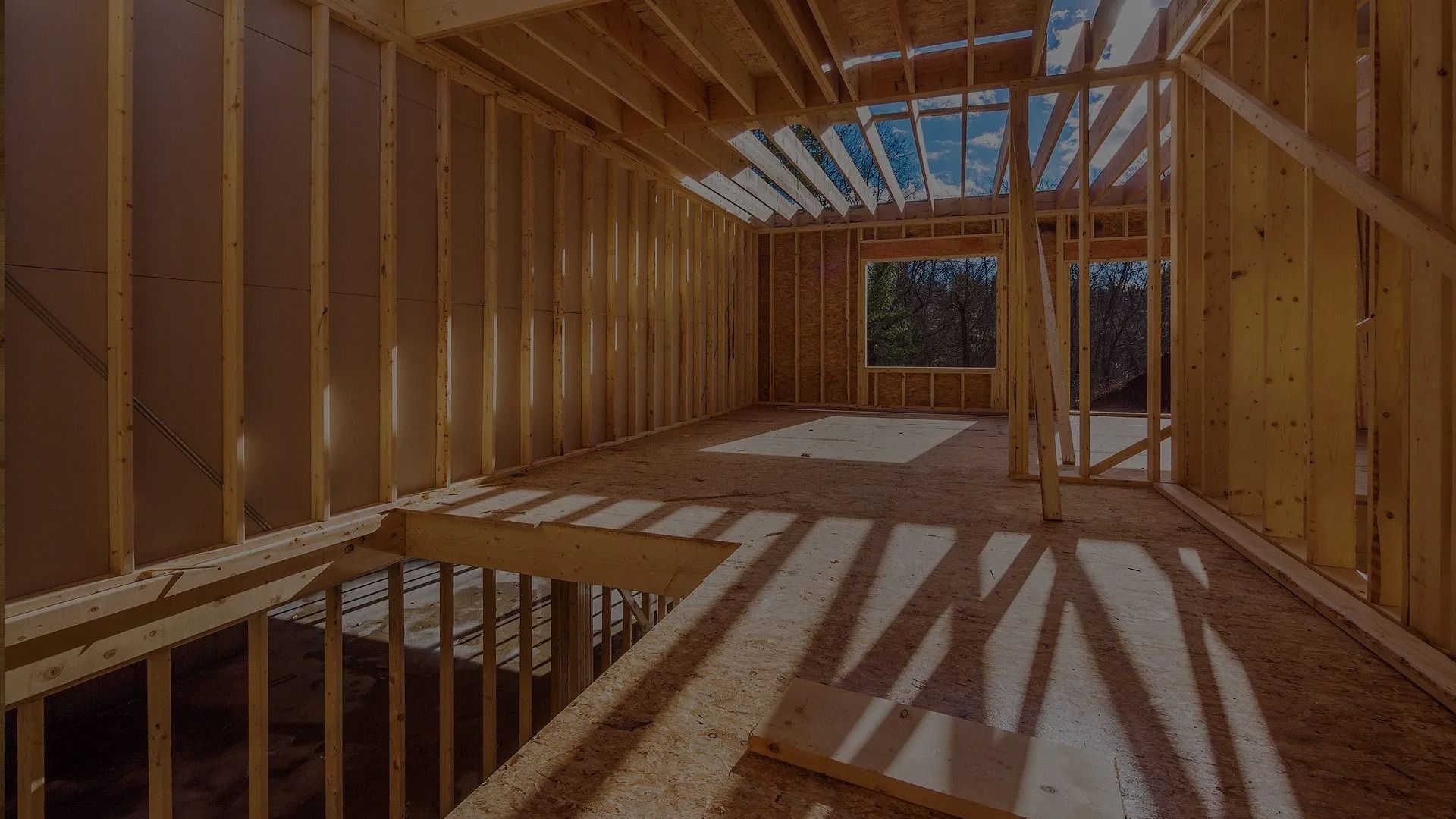 The interior frame of an unfinished house under construction, showing wooden wall studs, floor joists, and open rafters.