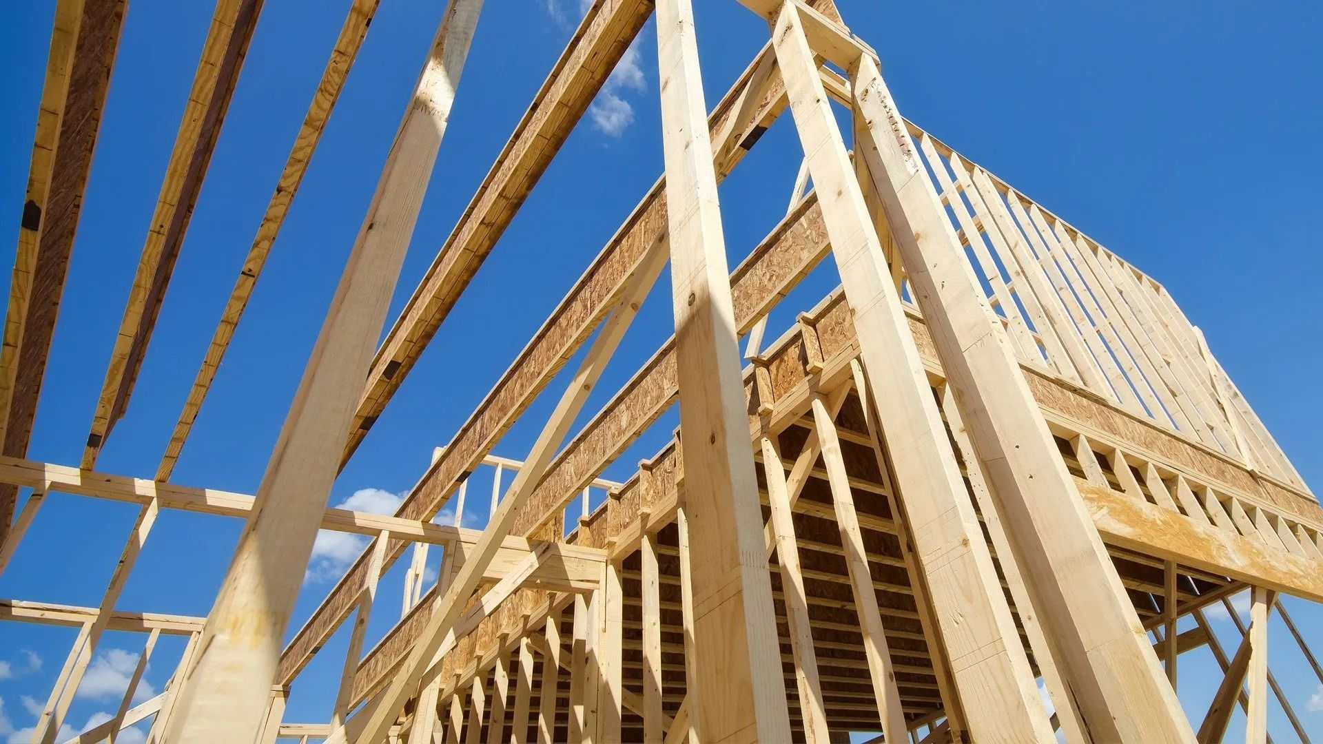 The wooden frame of an unfinished house under a clear blue sky.