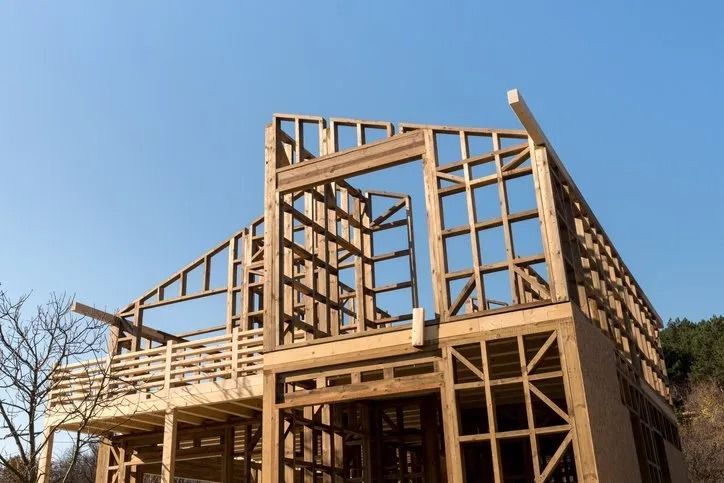 A wooden frame structure of a house under construction against a clear blue sky.