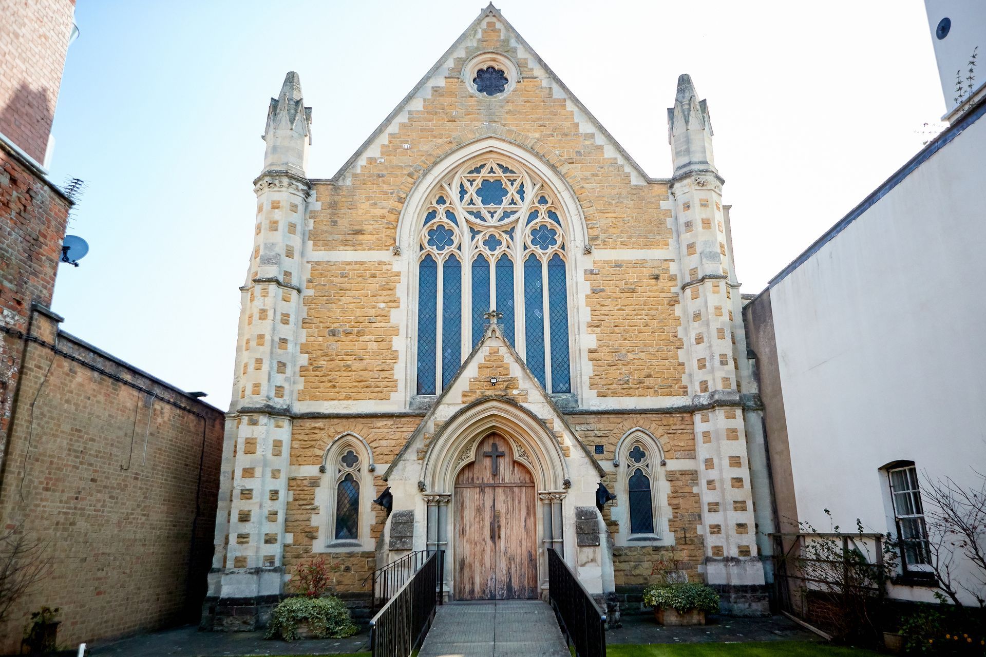 Tan stone church with arched doorway, large stained glass window, and decorative turrets.