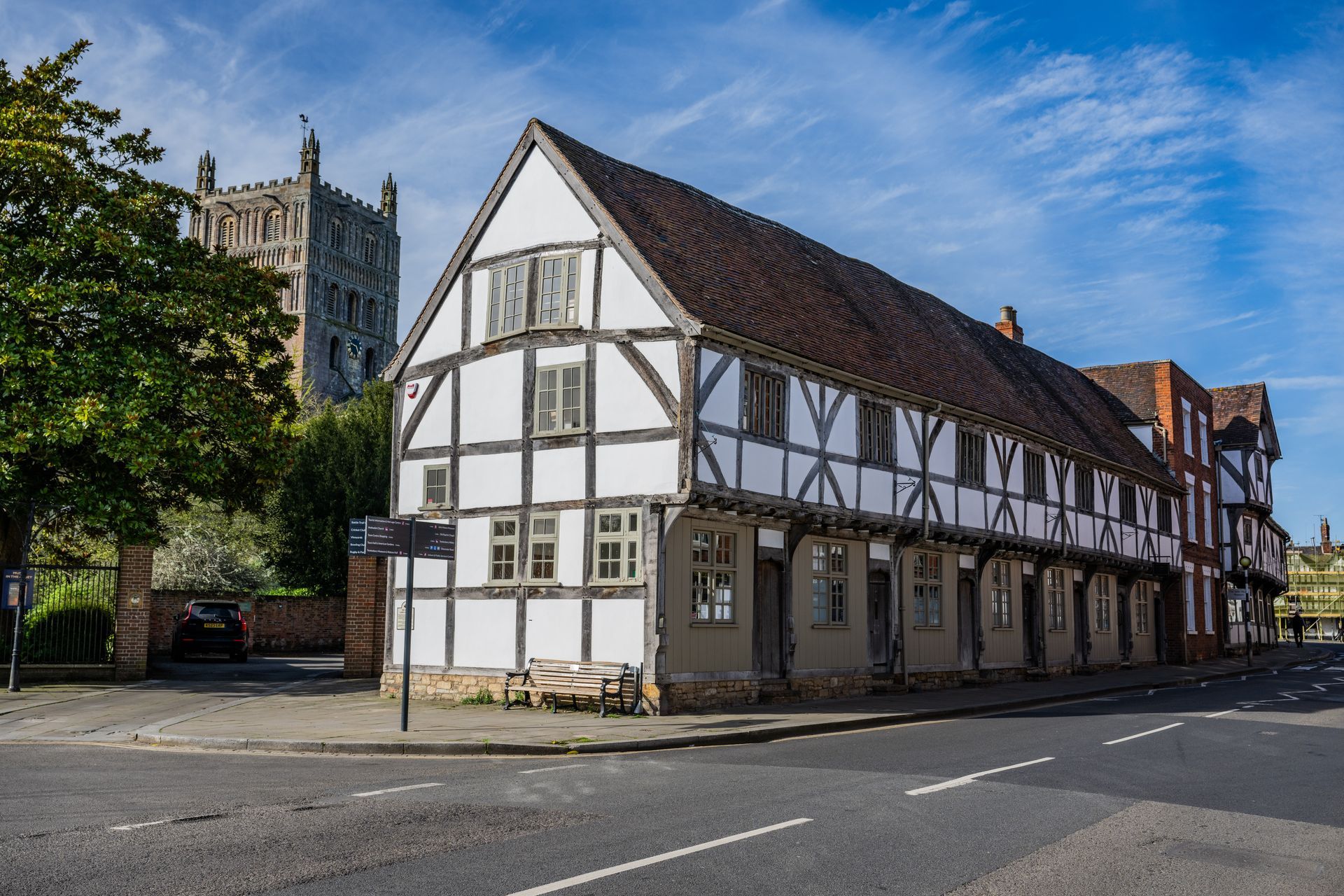 Tudor-style building with white and black timbers, next to a street, a church tower in the background.