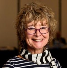 Woman with curly hair and glasses smiles; wearing striped shirt and scarf.